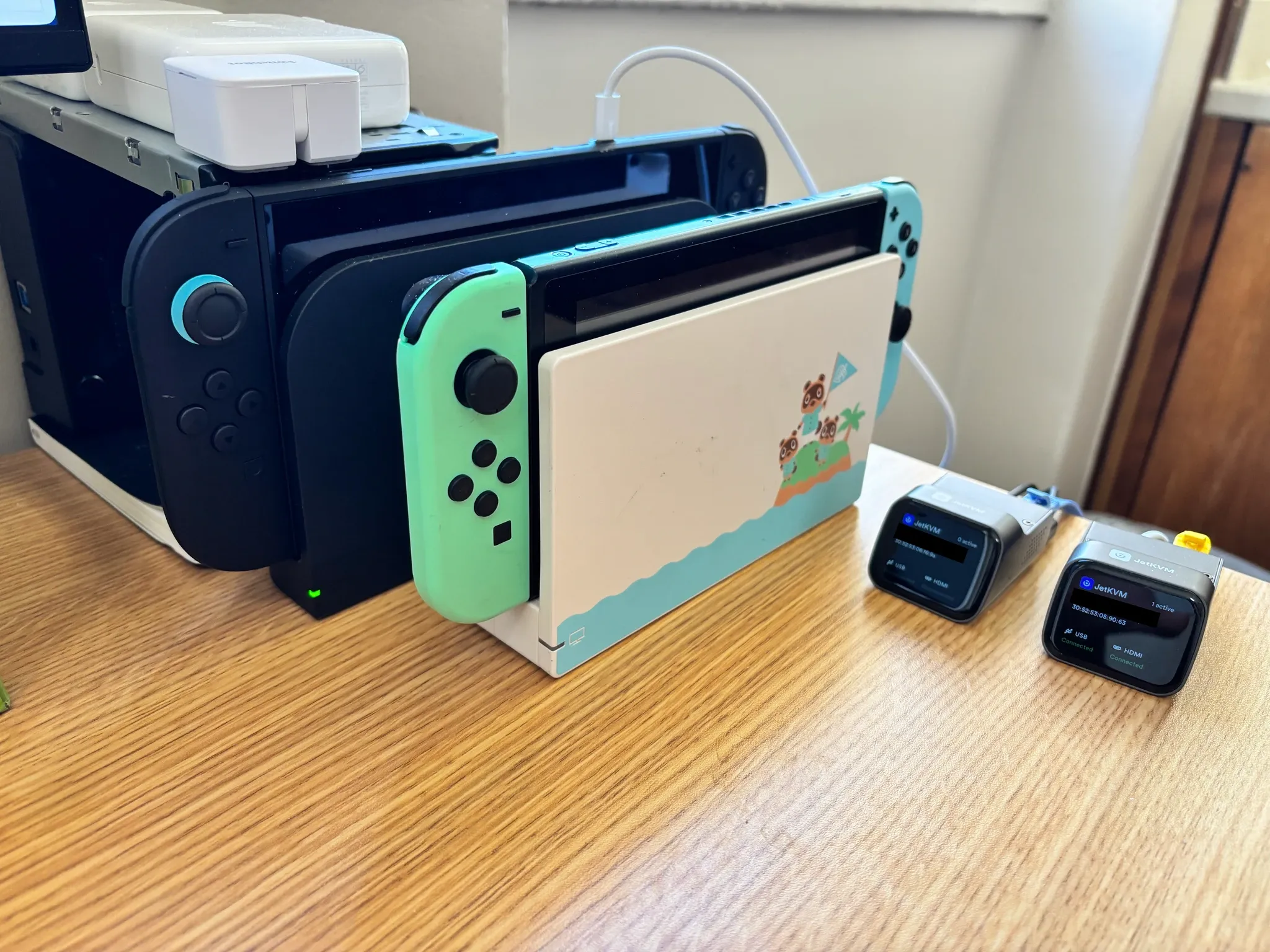 一台 Switch 1 和一台 Switch 2 放在木桌上，旁边是两台 JetKVM 和一台 SwitchBot
